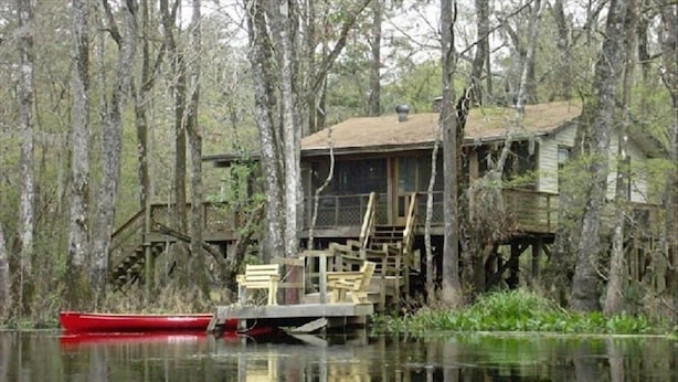 A houseboat with a deck and stairs, surrounded by trees and water. - Relax on a Beautiful River in a Natural Florida Setting (Tallahassee)