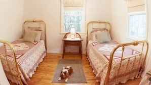 A room with two metal beds, a wooden floor, a ceiling fan, a window with curtains, and a small table with a lamp. - Relax on a Beautiful River in a Natural Florida Setting (Tallahassee)