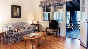 A cozy living room with a checkered sofa, a wooden coffee table, and a television on a stand. A framed picture hangs on the wall, and a window with a view of the outdoors is visible. - Relax on a Beautiful River in a Natural Florida Setting (Tallahassee)