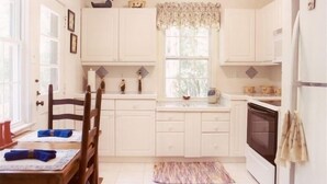 A kitchen with white cabinets, a window with a floral valance, a dining table with chairs, and a refrigerator. - Relax on a Beautiful River in a Natural Florida Setting (Tallahassee)