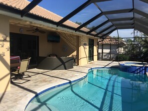 Una piscina scoperta coperta con un'area patio, una ventola a soffitto e un televisore fissato al muro.