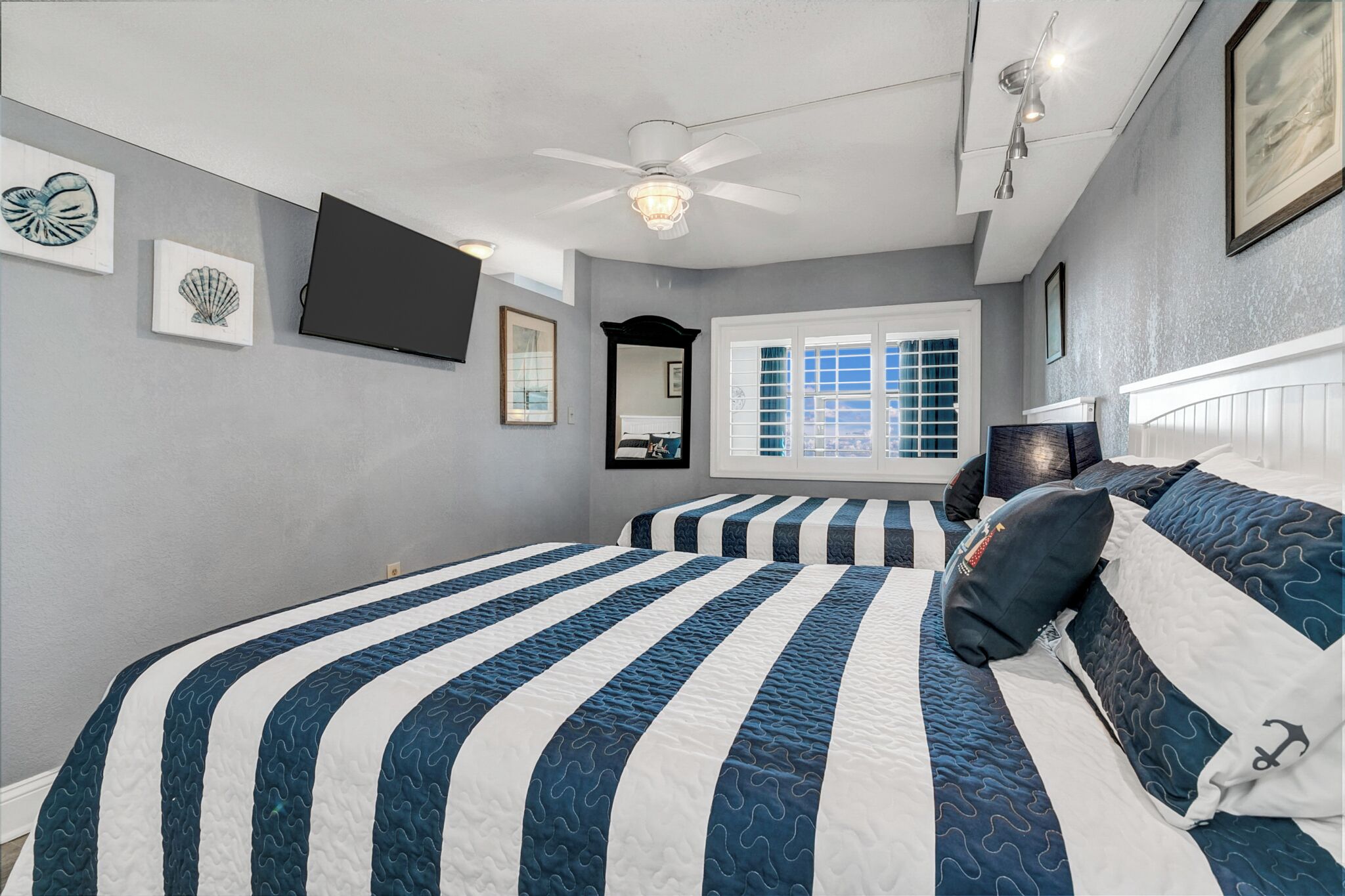 A bedroom with a large bed, a ceiling fan, a window with blinds, and artwork on the walls.