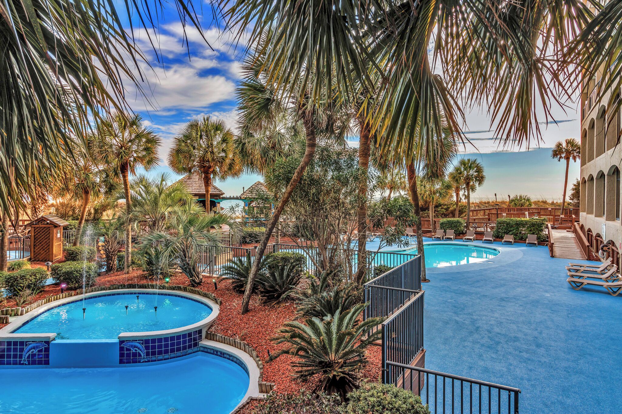 A pool area with multiple pools, palm trees, and a wooden deck.