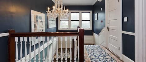 Classic design hallway with a wooden staircase, ornate chandelier, and patterned carpet.