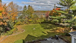 Ein angelegter Garten mit einer Steinterrasse, einem Grill und Blick auf einen See.