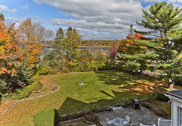 A landscaped backyard with a stone patio, a grill, and a view of a lake. - Spectacular Ocean Views, Walking Distance To Town, Bike Into Acadia (Bar Harbor)