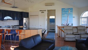 A spacious living area with a black leather sofa, a glass coffee table, and a beige recliner. A kitchen with dark blue cabinets and a stainless steel refrigerator is visible in the background. - Stay in the landmark Lighthouse! (Rock Hall)