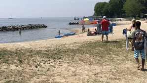 A beach with people, a sailboat, and a rocky breakwater. - Stay in the landmark Lighthouse! (Rock Hall)