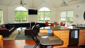 A spacious living area with a large window, a sofa, a coffee table, and a dining area with chairs and a kitchen island. - Stay in the landmark Lighthouse! (Rock Hall)