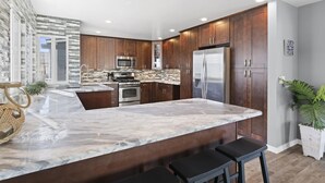 A modern kitchen with dark wood cabinets, stainless steel appliances, and a marble island with bar stools. - Stunning 6-Bedroom Oceanview Vacation Home w/ Rooftop Deck (Newport Beach)