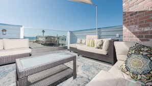 A rooftop terrace with a wicker sofa set, a glass-top coffee table, and a patterned rug. - Stunning 6-Bedroom Oceanview Vacation Home w/ Rooftop Deck (Newport Beach)