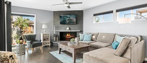 A modern living room with a fireplace, a ceiling fan, and a large window overlooking a garden.