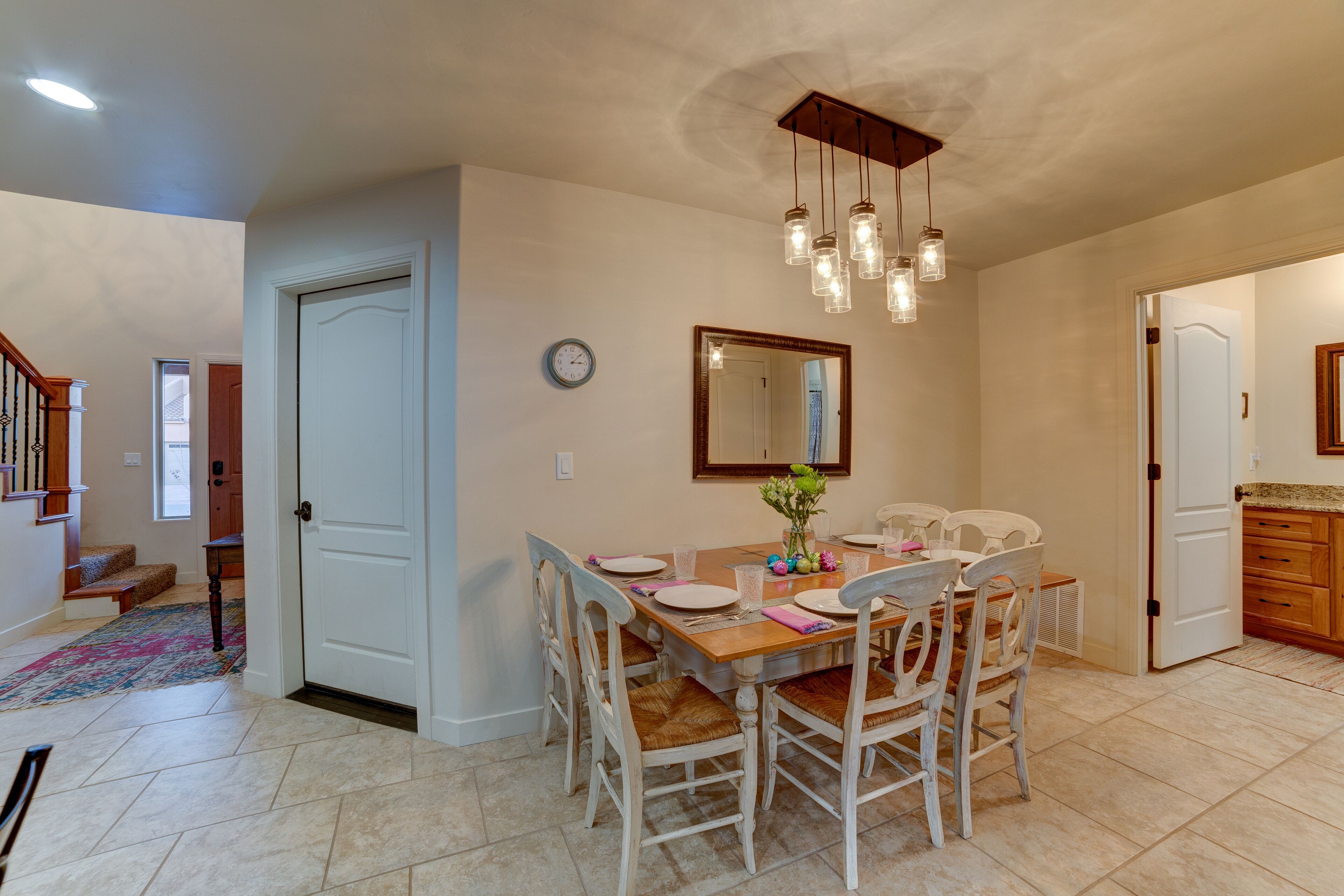 Un comedor con una mesa de madera, sillas blancas y lámparas colgantes.