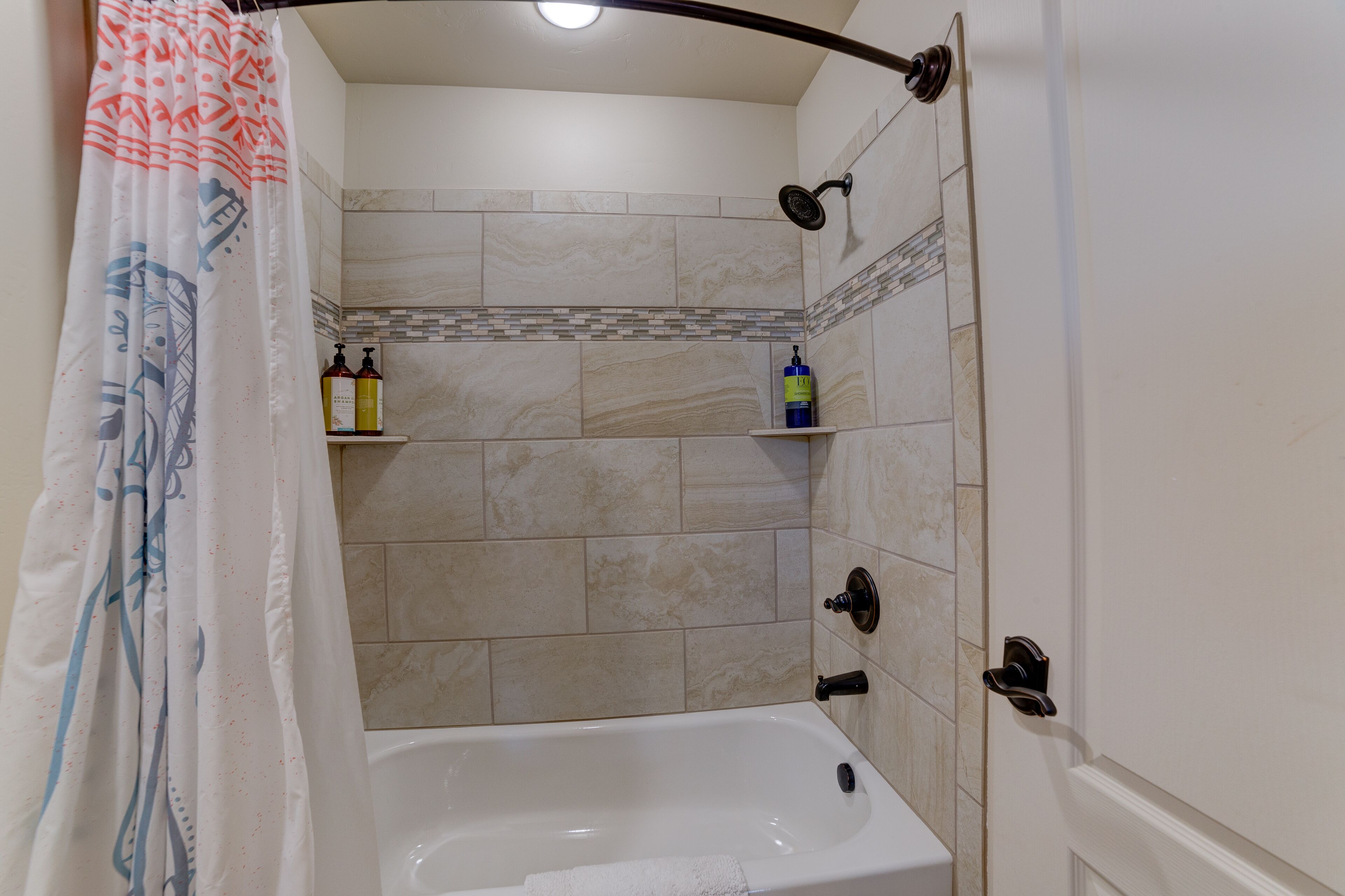 A bathroom with a bathtub, a shower, and a toilet. There are toiletries on a shelf.