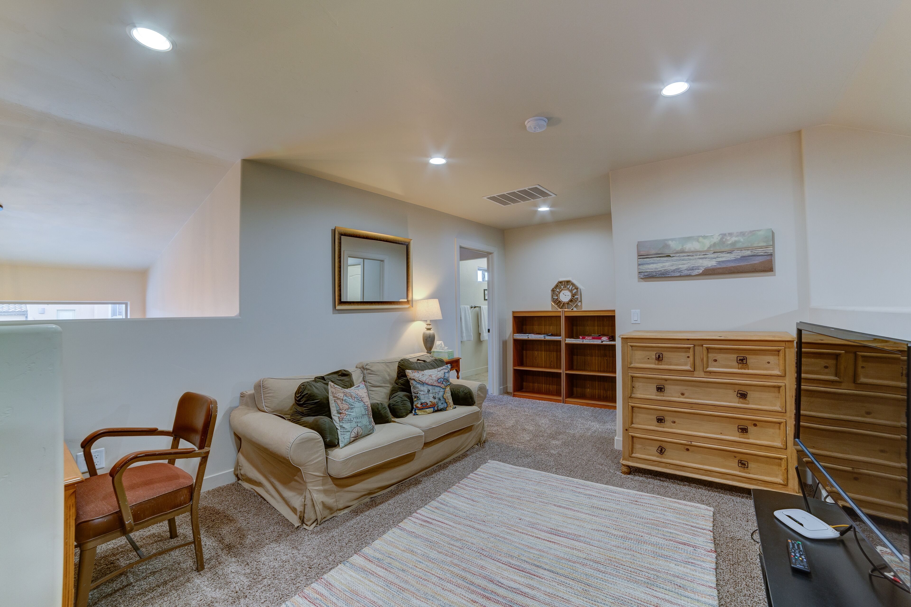 A living room with a sofa, a wooden chair, a desk with a computer, a dresser, and a painting on the wall.