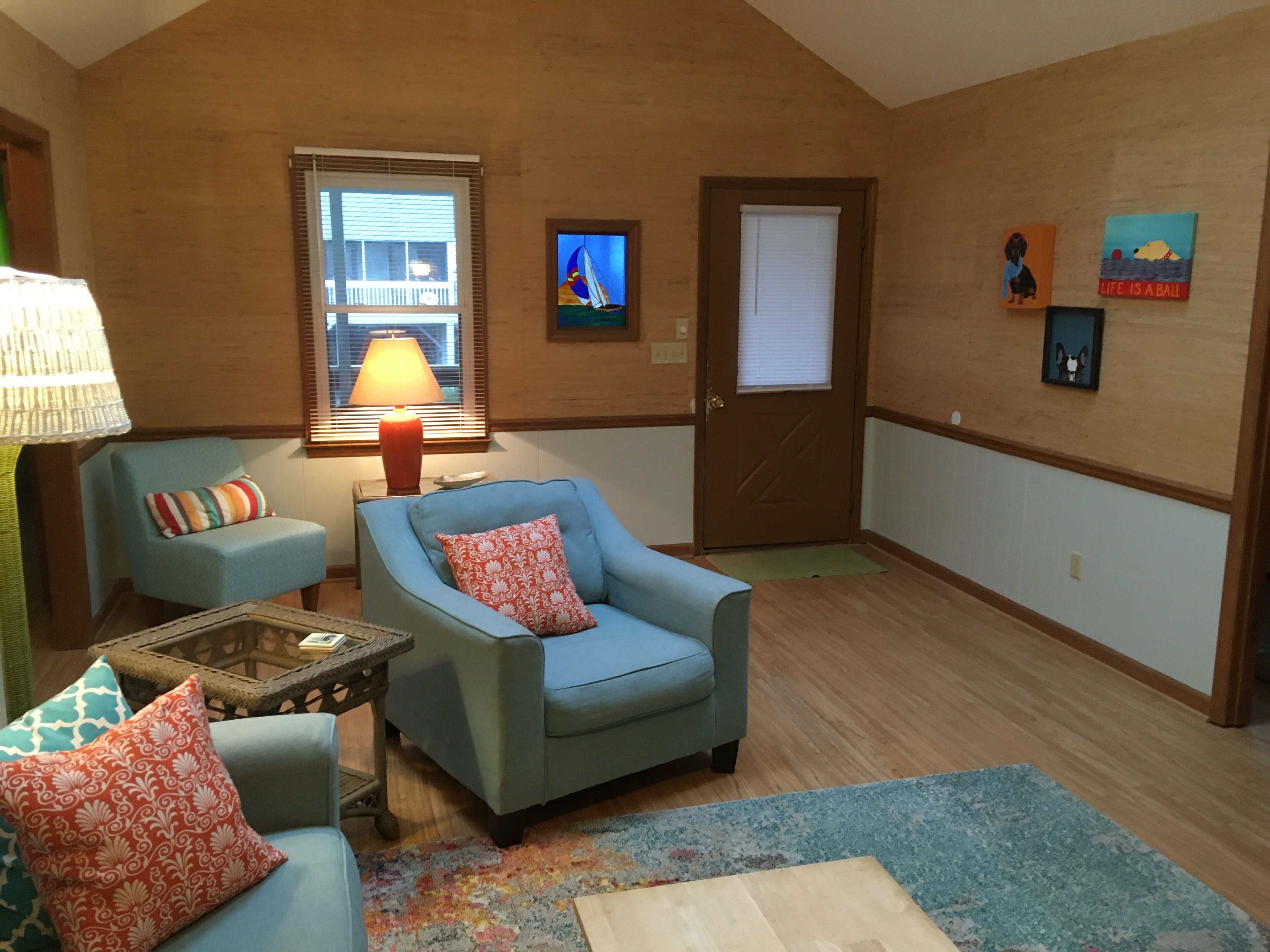 Uma sala de estar com dois poltronas, uma mesinha, uma luminária e uma porta.