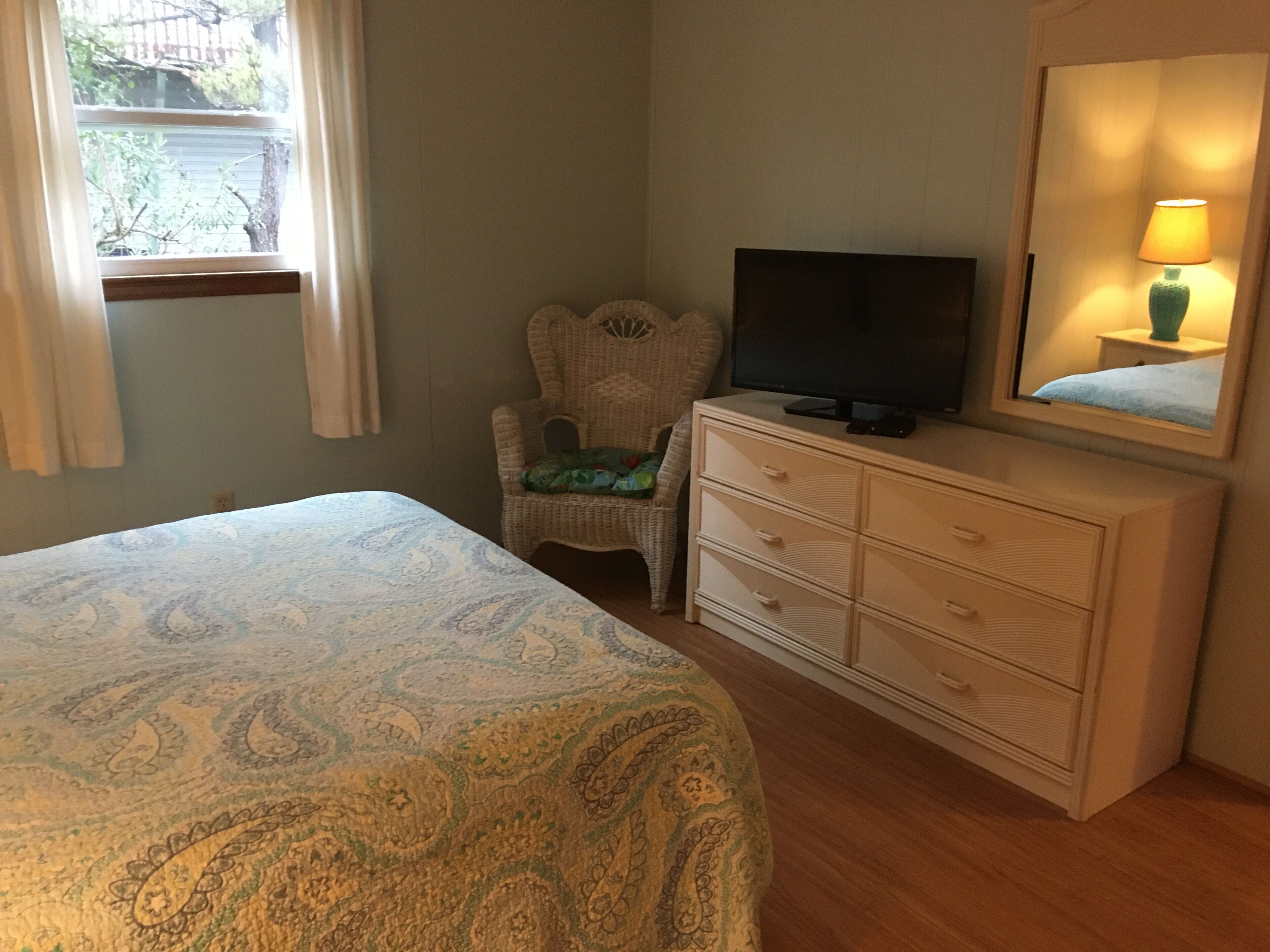A bedroom with a bed, a television on a dresser, a chair, and a window with curtains.
