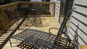 Una terraza de madera con una mesa y sillas de metal, una silla de metal y una barandilla de madera.