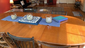 A dining area with a wooden table set for four, surrounded by chairs. There are three glass containers with a creamy substance on the table, and a blue notebook is placed on the table's right side. - Walk from your family friendly house to the beach, downtown, or Wychmere Resort (Harwich Port)