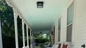 A covered porch with white railings, a brick pathway, and outdoor furniture including two rocking chairs and a table. - Walk from your family friendly house to the beach, downtown, or Wychmere Resort (Harwich Port)