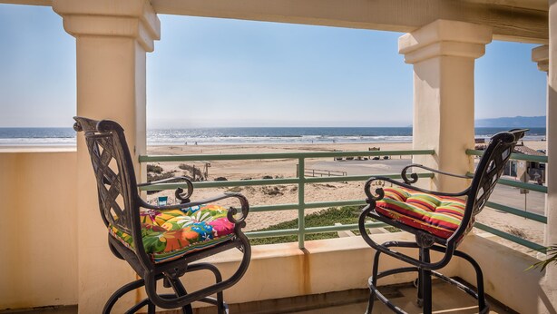 Ein Balkon mit zwei Stühlen, der auf einen Strand blickt.