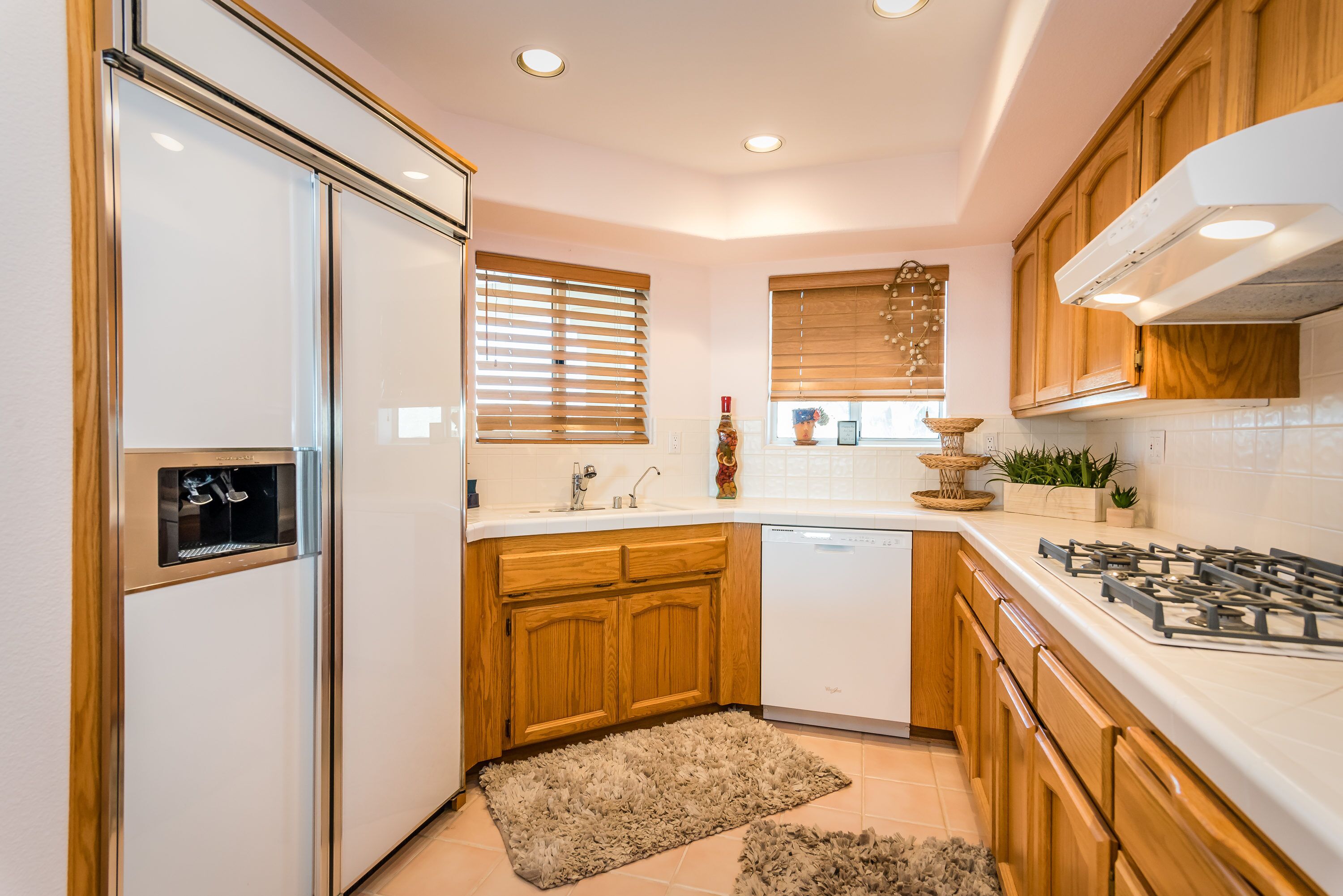 A modern kitchen with wooden cabinets, a built-in dishwasher, a gas stove, and a window with blinds.
