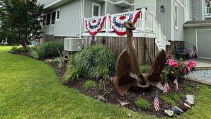 Una casa a due piani con un portico coperto, una grande scultura a forma di ancora e bandiere americane.