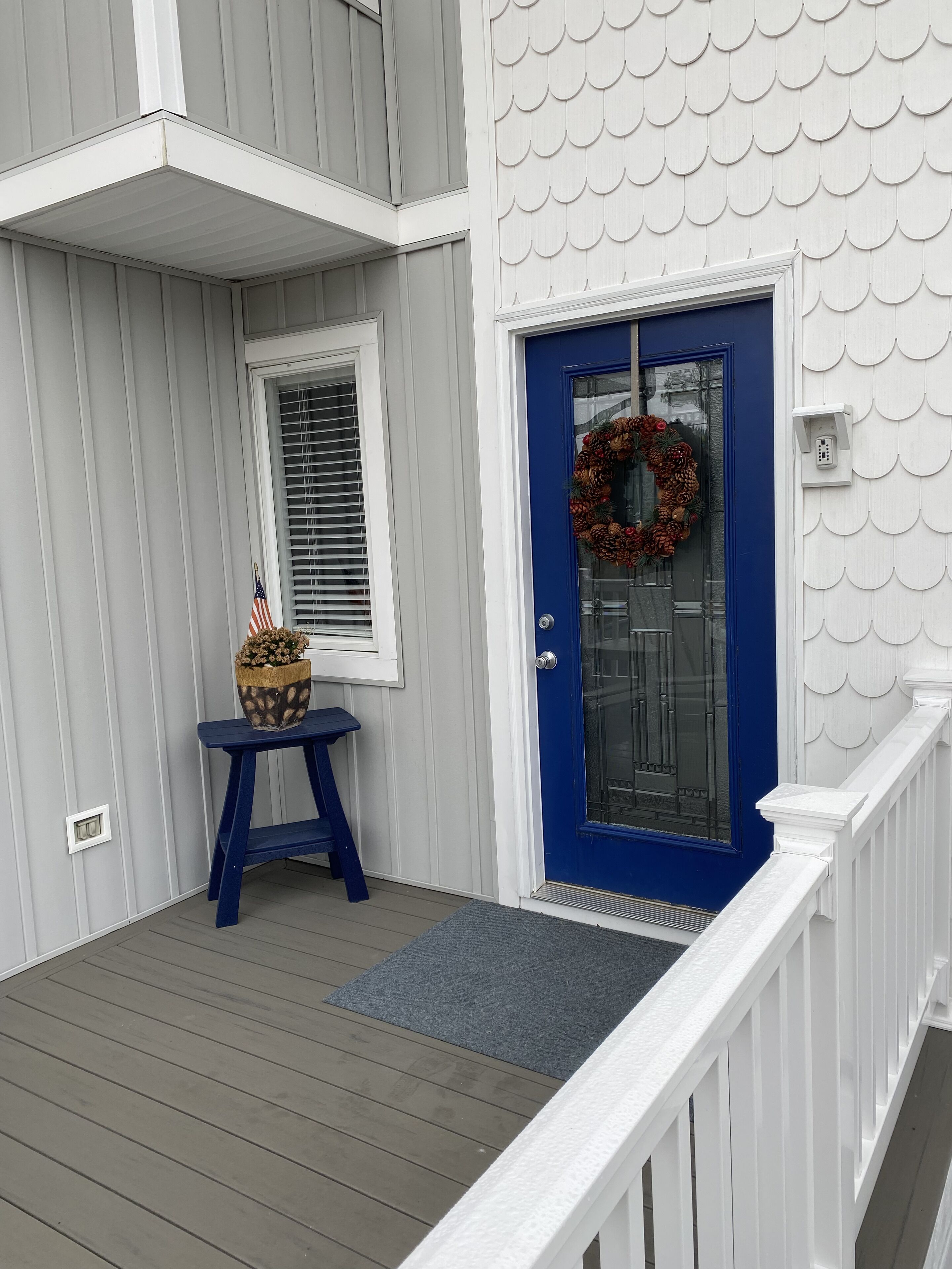 Une maison avec une porte d’entrée bleue, une guirlande et une petite table sur laquelle est posée une plante en pot.