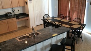 A kitchen with a central island, a sink, and a dining area with chairs.