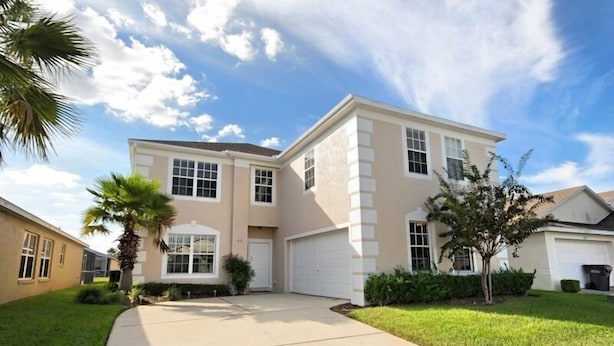 A two-story house with a garage, a front lawn, and a palm tree.