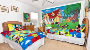 A bedroom with two beds, each with Mickey Mouse-themed bedding, a ceiling fan, and a mural of Mickey Mouse characters on the wall.