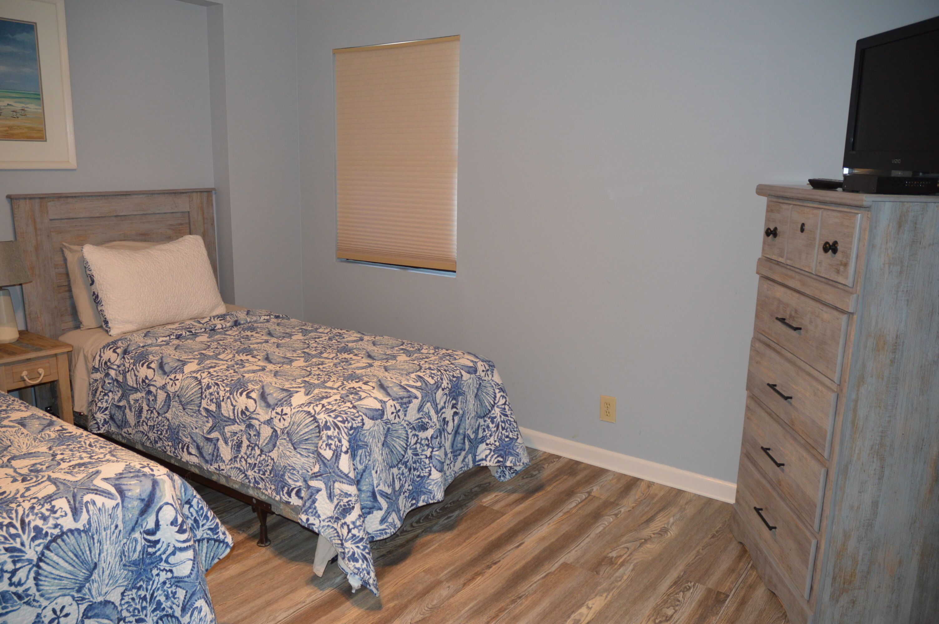 A bedroom with two beds, a dresser, a television, and a window with blinds.