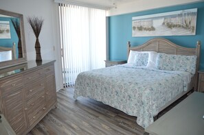 A bedroom with a wooden bed, a dresser, and a large window with blinds.