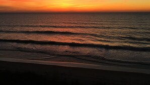 Een zonsondergang boven de oceaan met golven die de kust naderen.