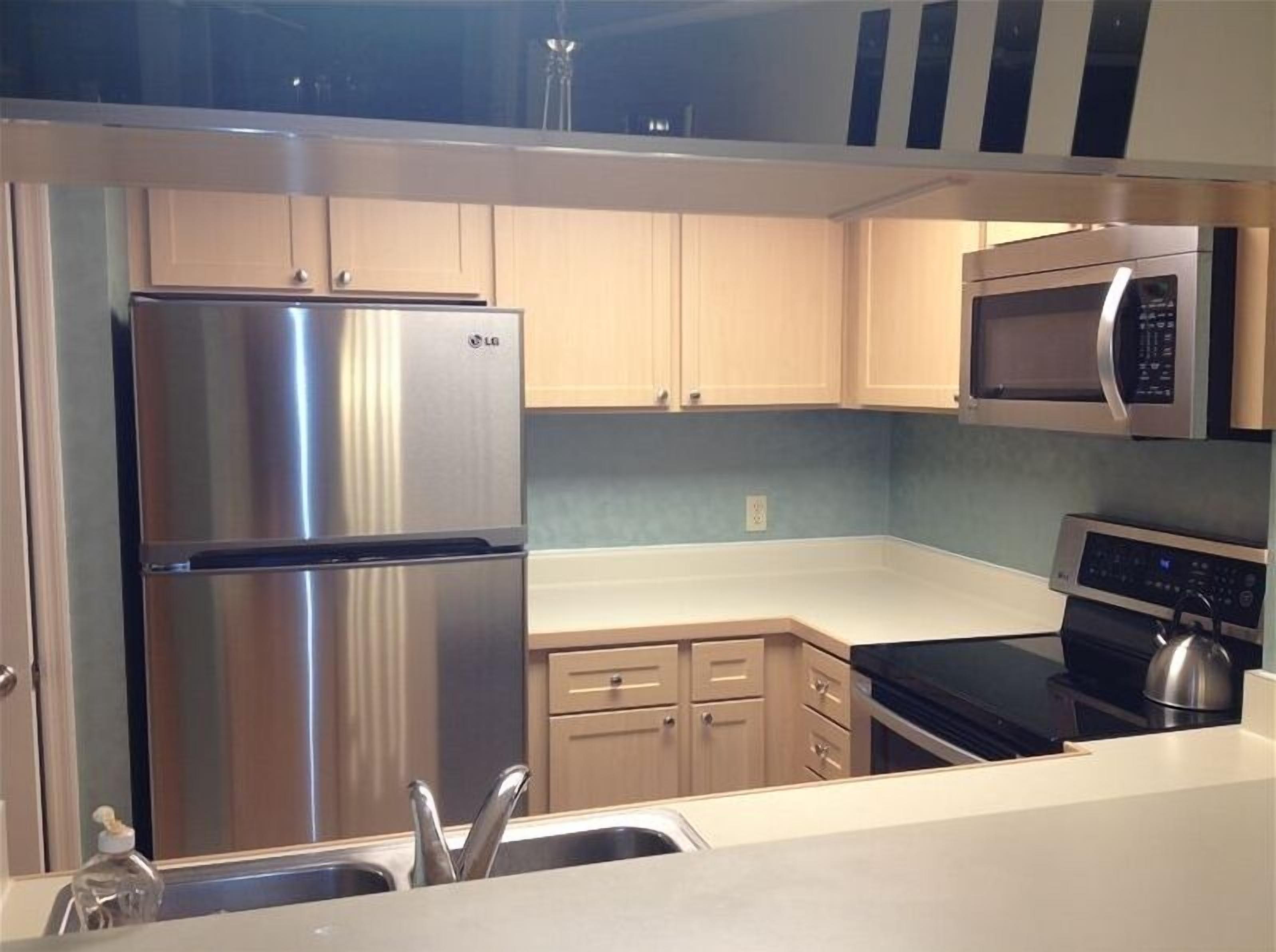 A modern kitchen with stainless steel appliances, light wood cabinets, and a black countertop.