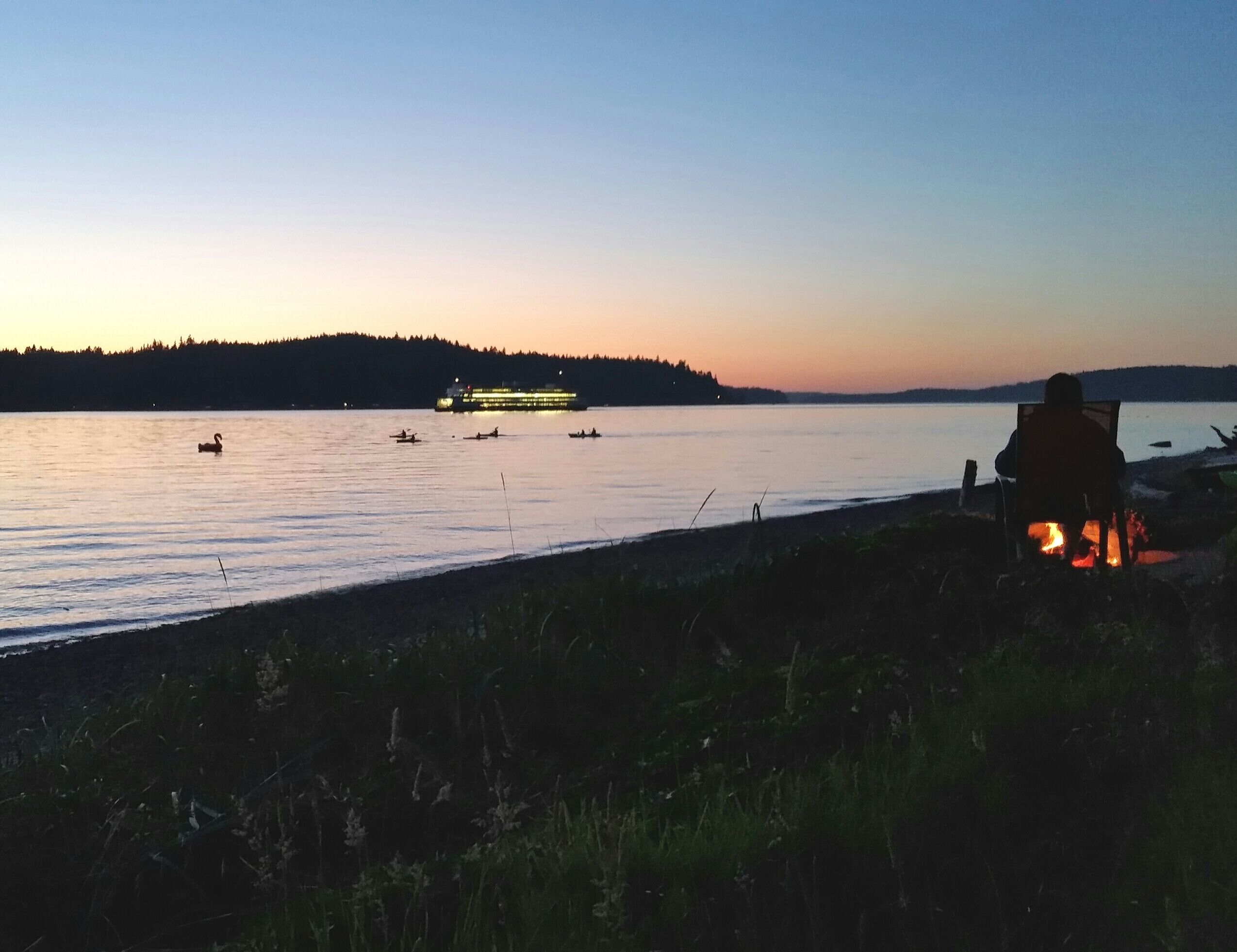 Beach fire at dusk with ferry and kayakers