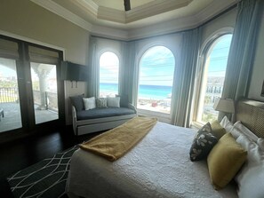 A hotel room with a bed, a sofa, and large windows offering a view of the beach and ocean.