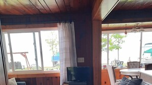 Ein Holzblockinterior mit grünem Teppich, Holzwänden, einer Couch, einem Tisch und einem Fernseher.