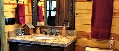 A wooden cabin bathroom with a granite sink, a mirror, a toilet, and a red towel hanging on the wall.