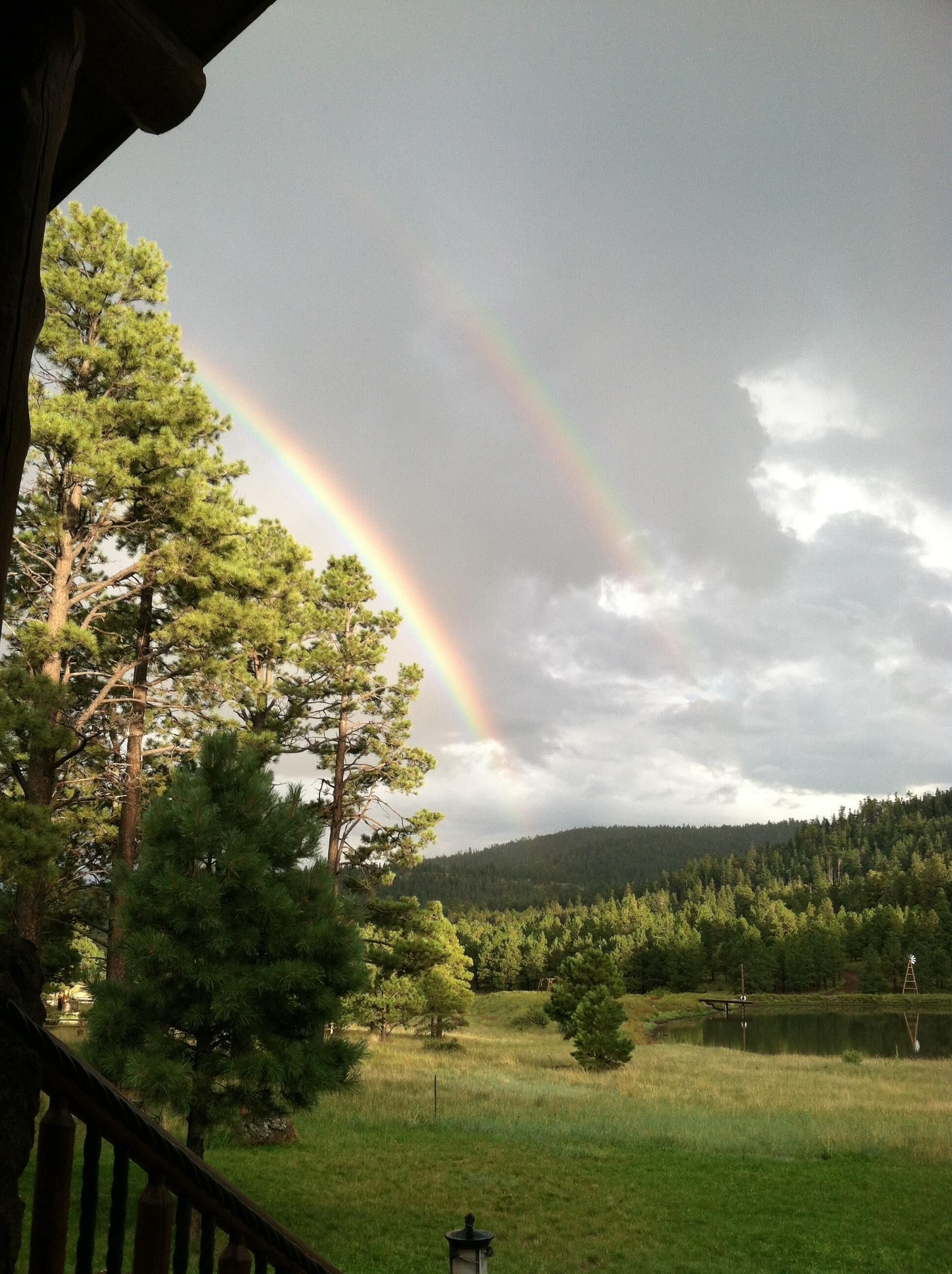 A view of a forested landscape with a rainbow and a wooden deck.