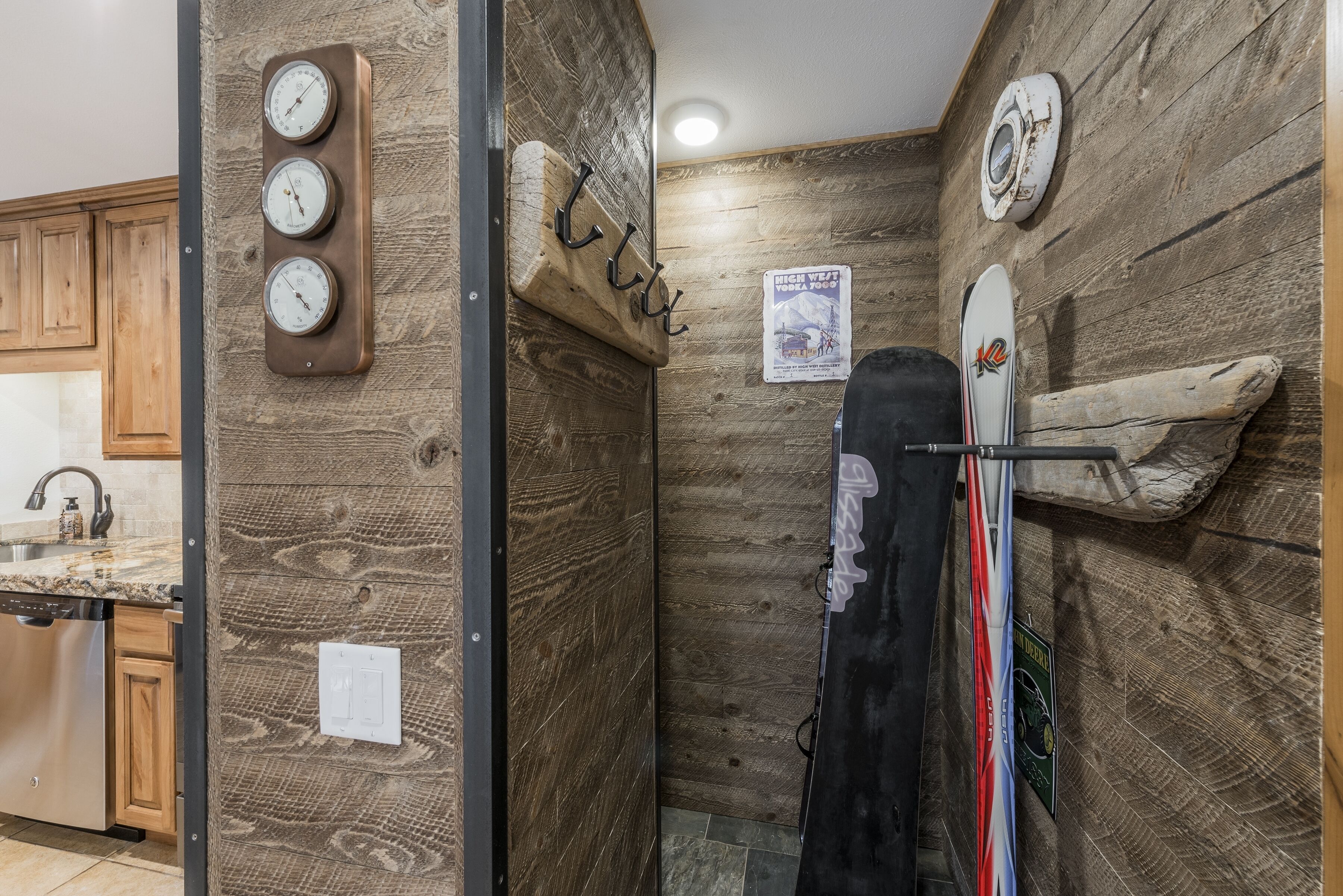 A kitchen with wooden cabinets, a granite countertop, and a dishwasher. There is a wall-mounted clock and a surfboard leaning against the wall.