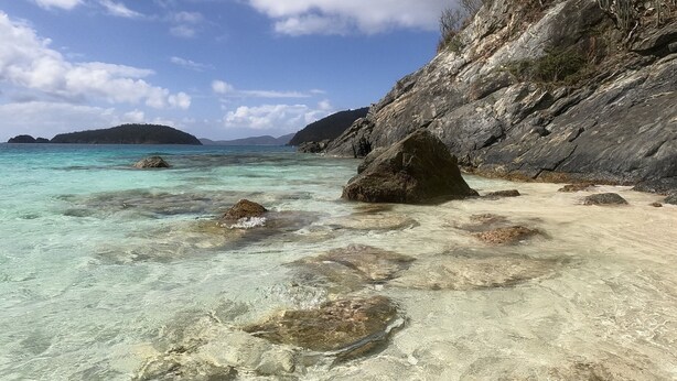 A beach with clear turquoise water, rocky shore, and a distant island.