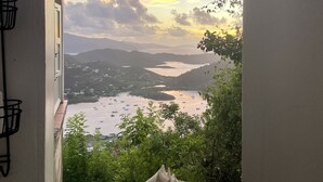 A view through a window with a seashell on the sill, overlooking a bay with boats and a sunset.