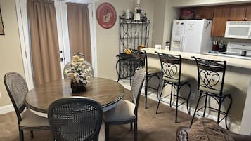 Un coin repas avec une table ronde, quatre chaises et un vase de fleurs. Il y a également un coin cuisine équipé d’un four à micro-ondes, d’un réfrigérateur et de placards.