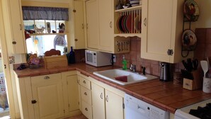 Una cocina con pileta, microondas y lavavajillas. Hay alacenas, un ventanal con cortinas y un salpicadero de azulejos.