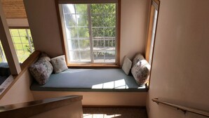 Un rincón acogedor con un banco acolchado, una ventana con vistas a la vegetación y techo de madera.