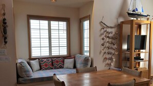 Un rincón comedor acogedor con una mesa y sillas de madera, un banco empotrado con cojines y un mueble de pared para la televisión.