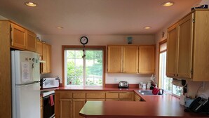 Una cocina con armarios de madera, un refrigerador, un microondas, un tostador y una ventana con vistas a zonas verdes.
