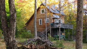 A wooden cabin with a porch and a staircase leading to a deck, surrounded by trees and a stone wall. - Beautiful Vacation Cottage with a View in Newfane, Vermont, near Mt. Snow (Newfane)