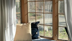 A room with a large bay window, a bed with a blue mattress and two pillows, and a view of a forested area. - Beautiful Vacation Cottage with a View in Newfane, Vermont, near Mt. Snow (Newfane)